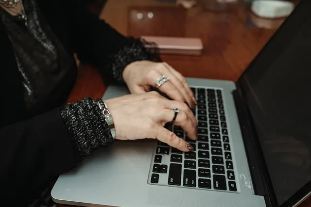 Photograph: Hands typing on a laptop at a wooden table during a casual indoor setting with a relaxed atmosphere.